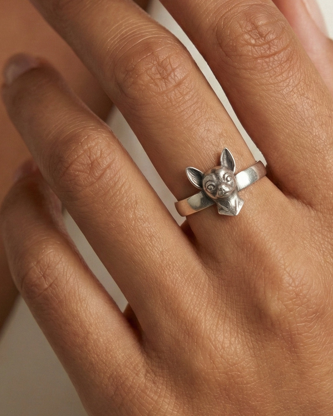 Silver Chihuahua dog ring on a person's finger with a white background