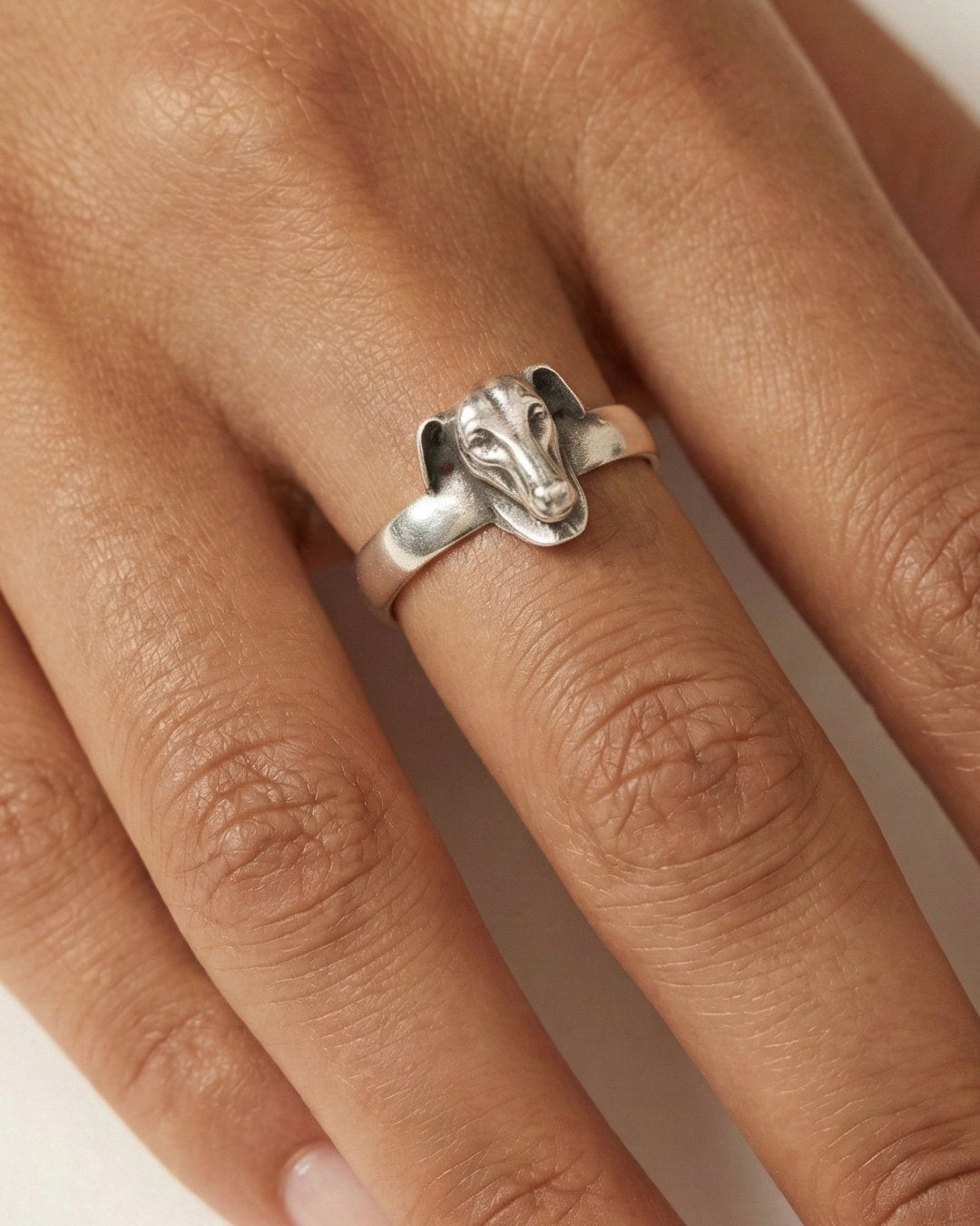 Silver Galgo dog ring on a person's finger with a plain background