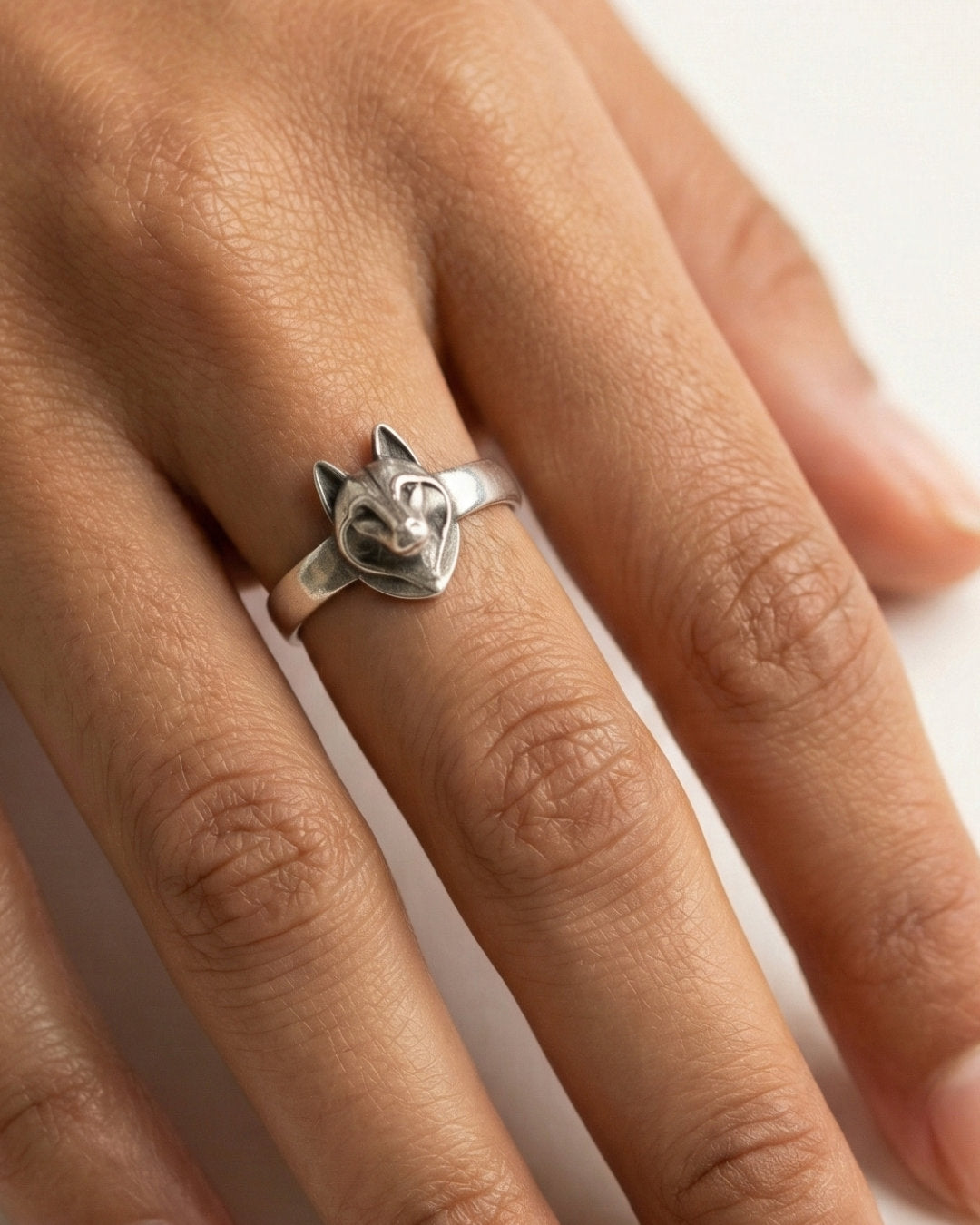 Silver Husky dog ring on a person's finger with a white background