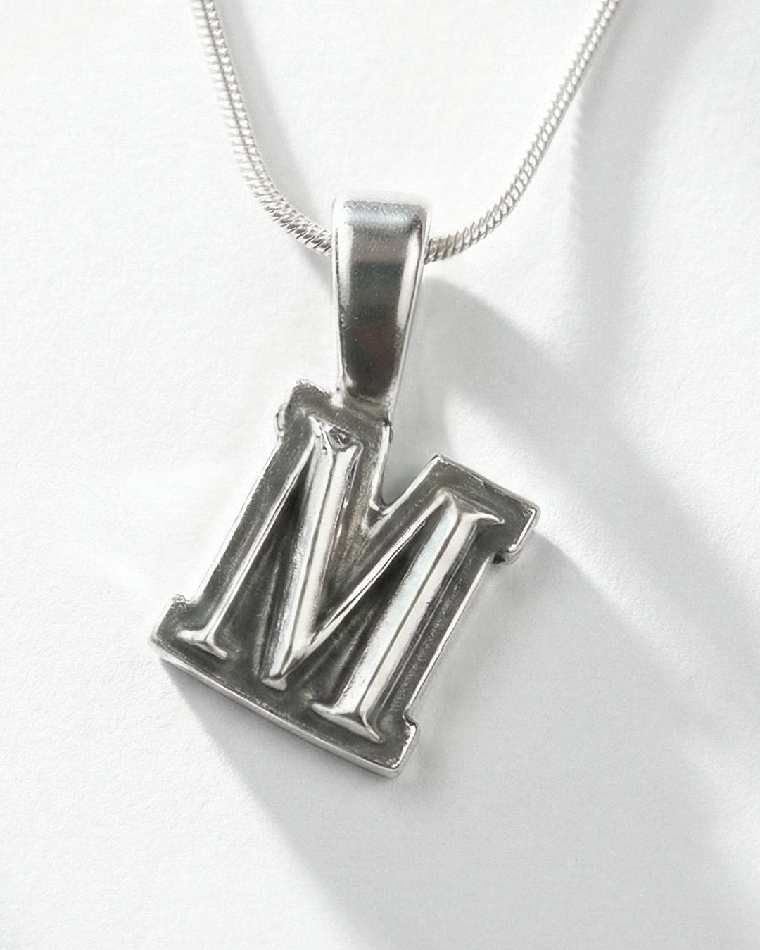 Silver pendant with the letter 'M' on a white background
